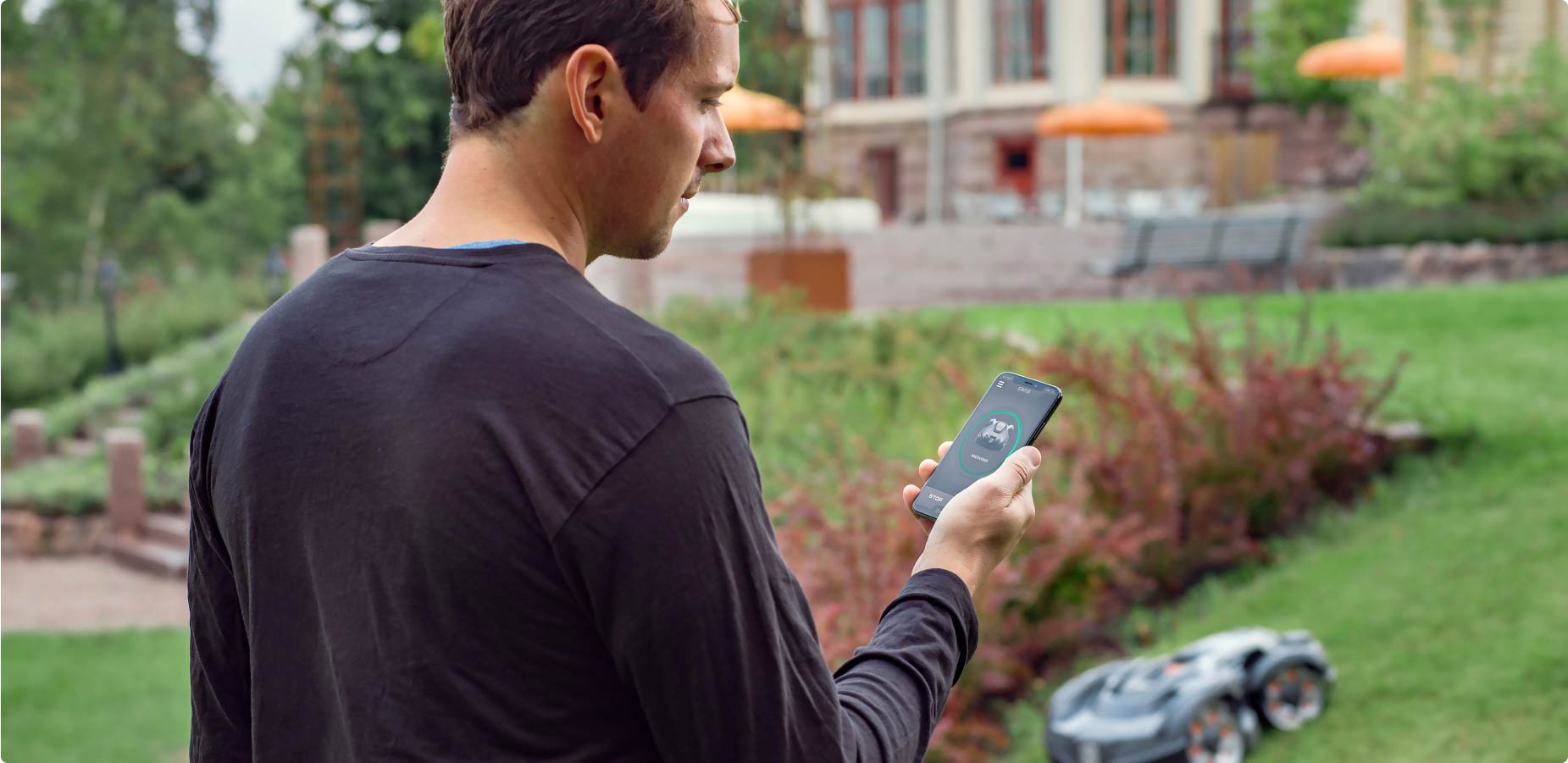 Man bestuurt Husqvarna robotmaaier in tuin via de app op zijn telefoon